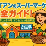 ホイアンのスーパーマーケットを背景に、買い物かごを持った女性と果物や野菜が並ぶ市場の様子を描いたポップなイラスト
